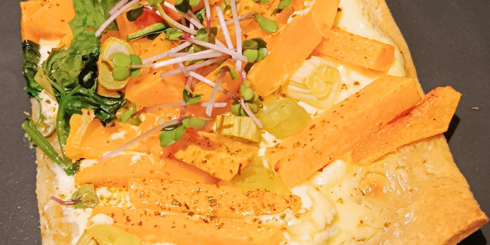 Ein Stück Pizza ist mit Kürbis und Keimsprossen belegt.