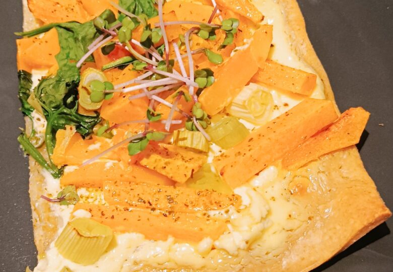 Ein Stück Pizza ist mit Kürbis und Keimsprossen belegt.