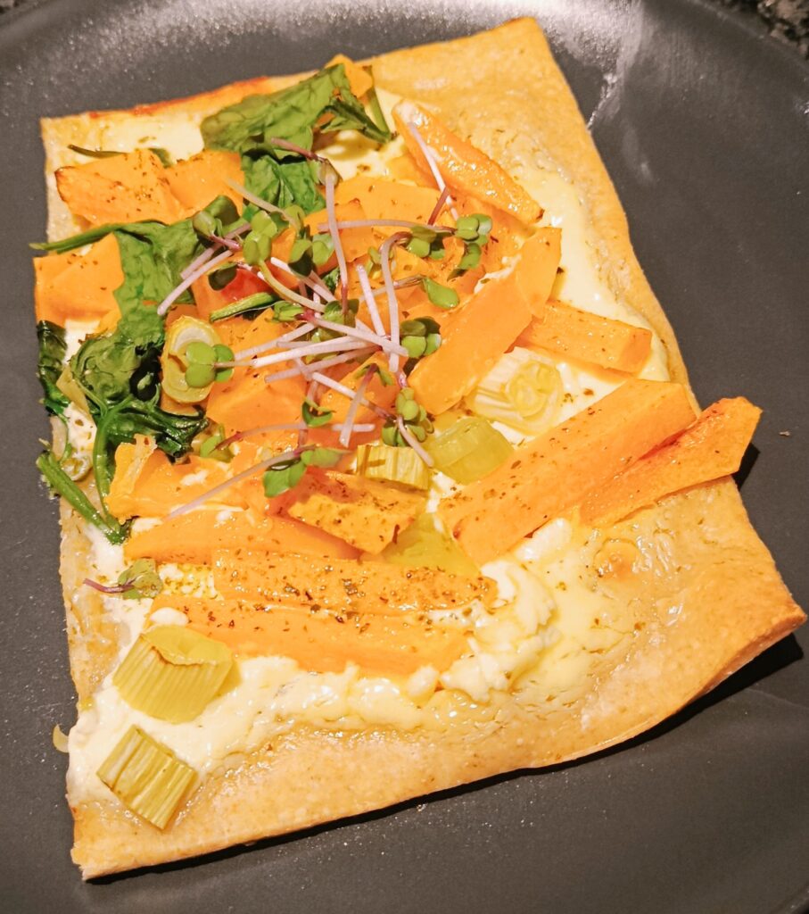 Ein Stück Pizza ist mit Kürbis und Keimsprossen belegt.